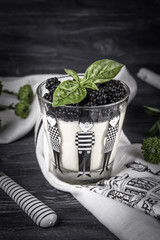 Homemade italian dessert panna cotta with fresh blackberries and green basil on a dark background