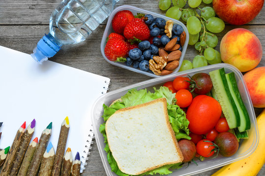 school lunch boxes with sandwich, fruits, vegetables and bottle of water with colored pencils