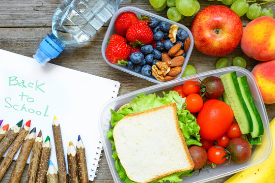 school lunch boxes with sandwich, fruits, vegetables and bottle of water with colored pencils and back to school inscription.
