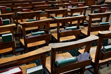 Rows of wooden empty chairs in a church with bibles and prayer books