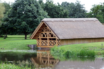Fototapeta na wymiar Pretty tudor style wooden framed thatch boathouse in a wood on the edge of a lake or river
