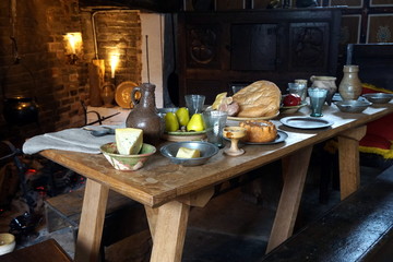 Rustic old wooden dining table in a medieval cottage, laid with bread, meat, cheese and fruit, and antique pottery and pewter