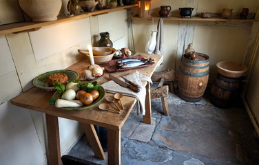 Rustic old wooden dining table in a medieval cottage, laid with meat, fish, eggs and fruit, and antique pottery and cutlery