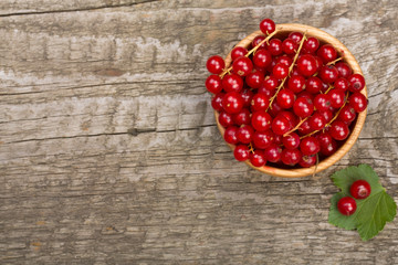 Red currant berries in a wooden bowl with leaf on the old wooden background. Top view