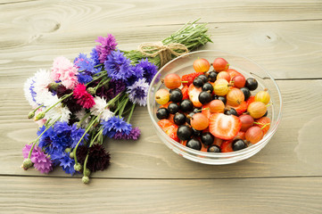 bowl full of fresh berries on the wooden background with flower cornflowers