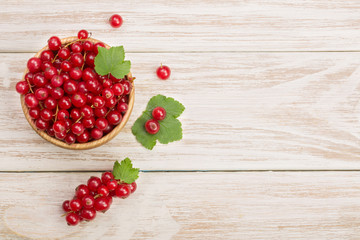 Red currant berries in a wooden bowl with leaf on the white wooden background. Top view