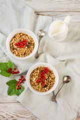 Summer healthy breakfast for two person of granola, muesli with milk jug with red currant decor on light wooden board. Top view.