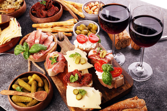 Italian antipasti wine snacks set. Cheese variety, Mediterranean olives, pickles, Prosciutto di Parma, tomatoes, artichokes and wine in glasses