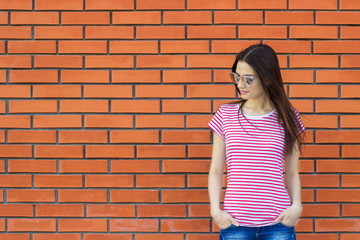 Attractive woman wearing striped t-shirt and fashionable sunglasses posing against red brick wall, swag street style. Empty background