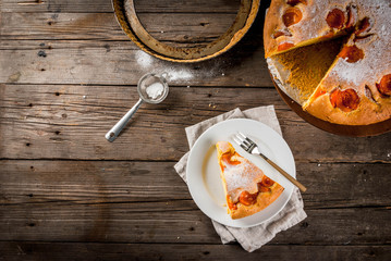 Homemade autumn and summer baked pastries. Sponge cake with apricots. Cut into pieces, plate, fork. On the stand. On the old wooden rustic table. Copy space top view