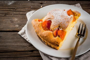 Homemade autumn and summer baked pastries. Sponge cake with apricots. Cut into pieces, plate, fork. On the old wooden rustic table. Copy space