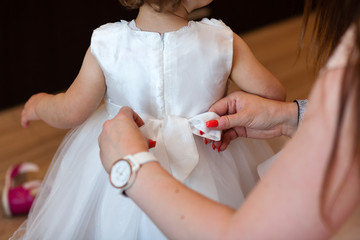 Fragment photo of little baby girl preparing for christening ceremony, hand on a white dress, baby girl on christening day.