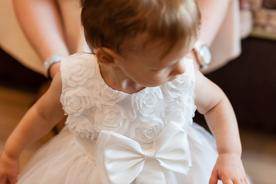 Fragment photo of little baby girl preparing for christening ceremony, hand on a white dress, baby girl on christening day.