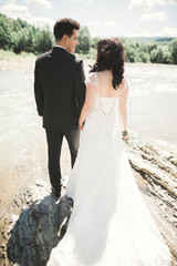 Beautifull wedding couple kissing and embracing near the shore of a mountain river with stones