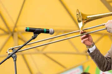 brass band, musical instrument and orchestra concept - closeup hands of male man playing trombone to external microphone on yellow background, performance of musician in concert suit, selective focus
