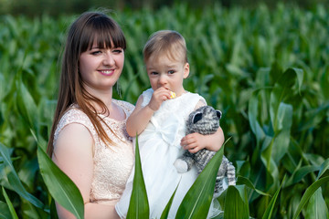 Funny baby girl in white dress is playing with mother  in the garden at christening