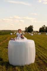 Funny baby girl in white dress is playing with mother on the hay bale at christening