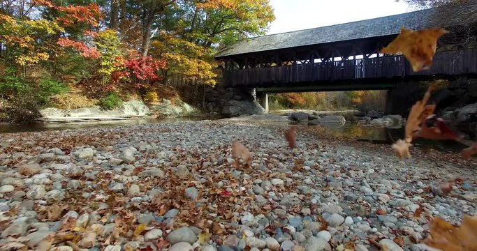 Covered Bridge Over Stream Bed with Leaves Blowing - Aerial Footage in Oxford, Maine, USA