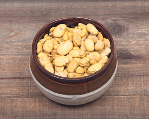 Organic dry broad haba beans in ceramic bowl on wooden vintage background