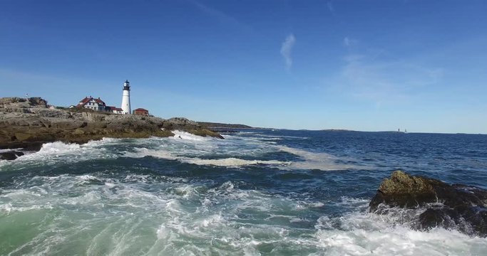 Lighthouse with Waves Breaking on Rocky Coast on the Atlantic Ocean Under a Blue Sky - Aerial Footage of Portland Head Lighthouse, Maine