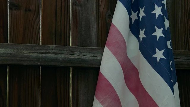 US Flag is hanging on fence, the wind blows it up and out of the frame, the flag returns and settles.
