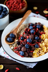 Healthy breakfast of cornflakes, chocolate balls, oatmeal, goji berries and fresh blueberries.