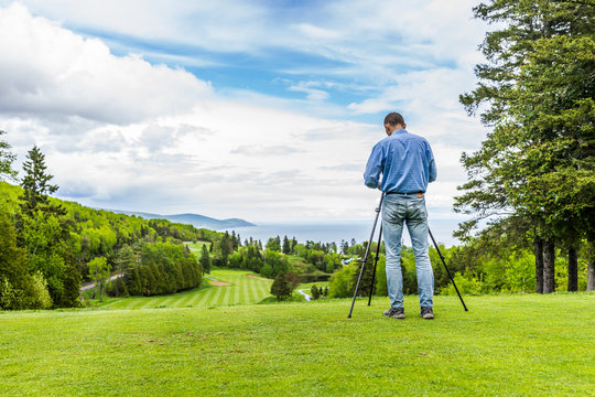 Landscape view of green golf course with hills in summer in La Malbaie, Quebec, Canada in Charlevoix region with photographer and tripod