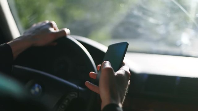 Man driver using smart phone car mobile driving steer steering wheel holding hand hands black display touching screen typing danger busy communication lifestyle blank calling finished talk sunny day