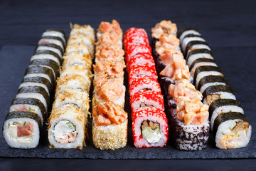 Appetizing multicolored sushi set on black slate, close-up. Traditional japanese food, restaurant serving