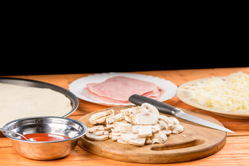 Sliced mushrooms on the round wooden board with sliced ham and cheese in the background