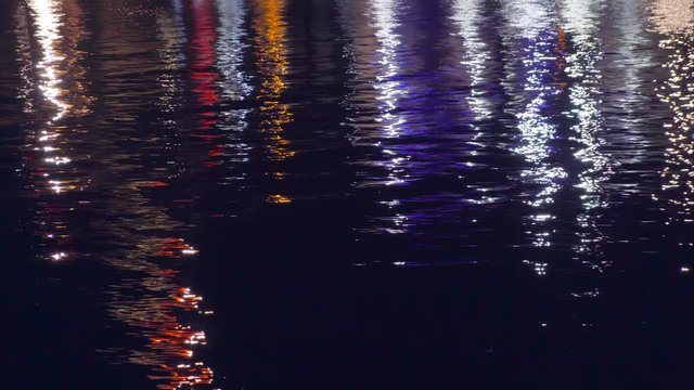 City seaport at night. Sea surface. Reflection of bright spotlights on the water surface. Quiet ripples. Float lights