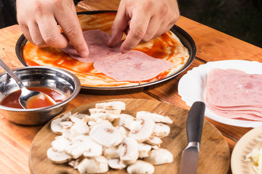 Table with ingredients for preparing pizza. Sliced mushrooms ham bowl with ketchup