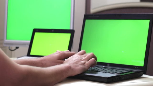 Add to Collection Businessman Working on a Laptop with Green Screen on. Man's Hands on the Table with Green Screen Laptop. Three monitors with a green screen. Many monitors..