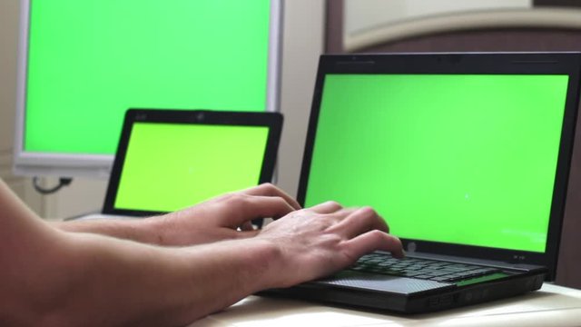 Add to Collection Businessman Working on a Laptop with Green Screen on. Man's Hands on the Table with Green Screen Laptop. Three monitors with a green screen. Many monitors..