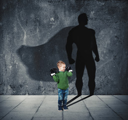 Young child with his shadow of super hero on the wall.