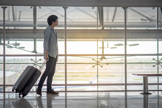Young Asian man walking in the airport terminal with suitcase luggage, travel lifestyle