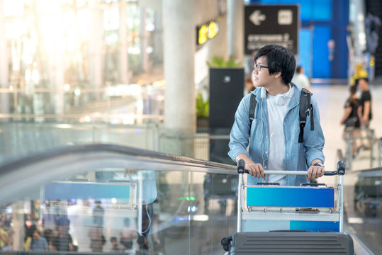 Young Asian man with airport trolley on escalator, walking to check-in counter in the international airport terminal. travel abroad on vacation