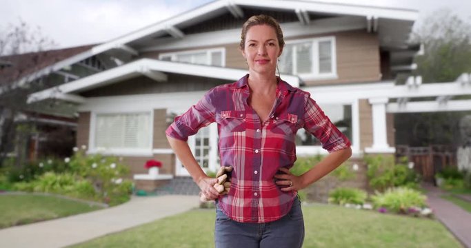 Woman with gardening gloves standing in front yard of home, dressed casually