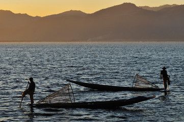 Silhouette of Burmese fisherman on boat catching fish in traditional way in Inle lake, Myanmar (Burma), Myanmar travel attraction landmark