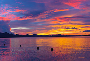 Dramatic cloudy sunset on a tropical island, Philippines. Sunset over calm sea waters and mountain ridges on the horizon.