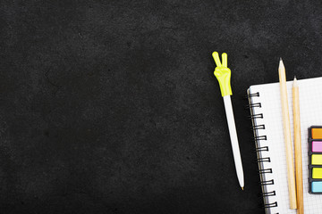 Stationery accessories: a notebook for notes, colored stickers, pencils, a pen with a cap with the symbol of a thumbs-up and an okay on a dark coal background. Top View.