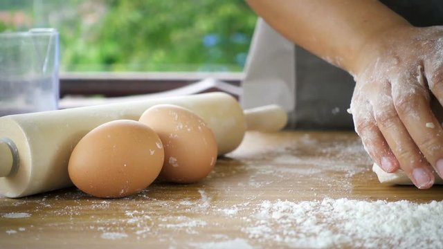 Female hands kneading dough in flour with green tree blurred background