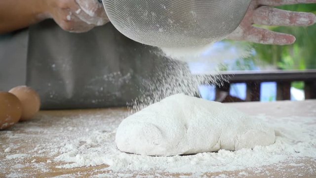 Close-up of flour through a metal sieve fray in nature blur background. Ingredients and preparation stages. Slowmotion shot