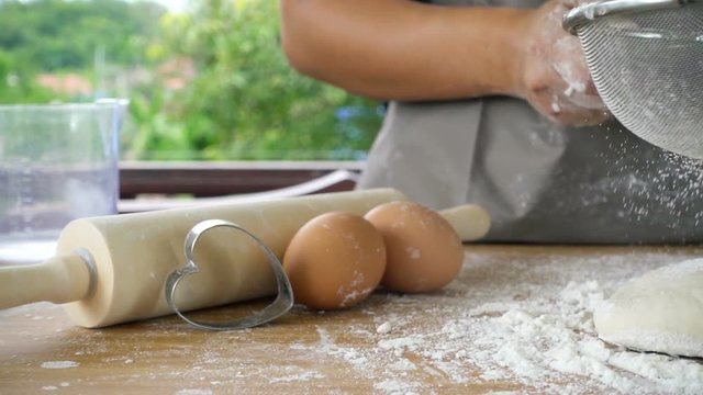 Close-up of flour through a metal sieve fray in green nature blur background. Ingredients and preparation stages. Slowmotion shot