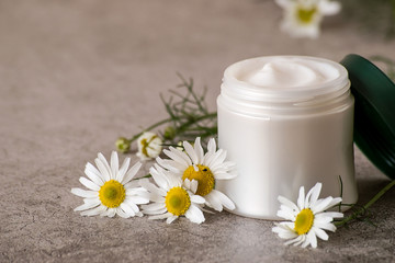 Fototapeta na wymiar Natural cosmetics. A jar with cream for face and body skin care and fresh chamomile flowers on a gray background.