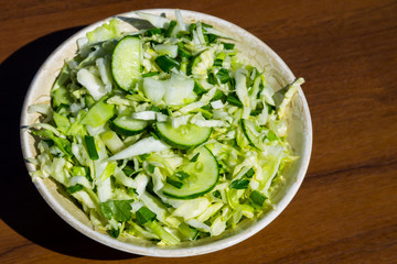 Spring vegan salad with cabbage, cucumber, green onion and parsley on wooden table