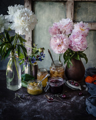assorted jams in jars with fresh cherries, spoon, peonies and blue textile on a brown table