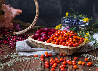 assorted autumn berries in basket and in a plate with dry herbs, flowers and textile on a brown wooden table
