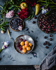assorted berries, apricots and flowers in plates on a grey background with grey textile, top view
