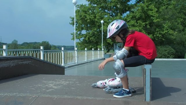 A child is putting on a roller. Little girl wearing a helmet dresses a roller skate.